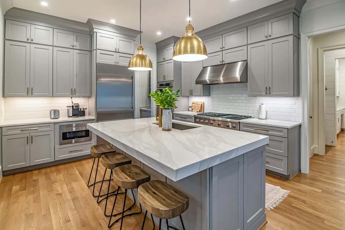 Completed kitchen remodel with marble island, gray cabinets, and gold pendant lights.